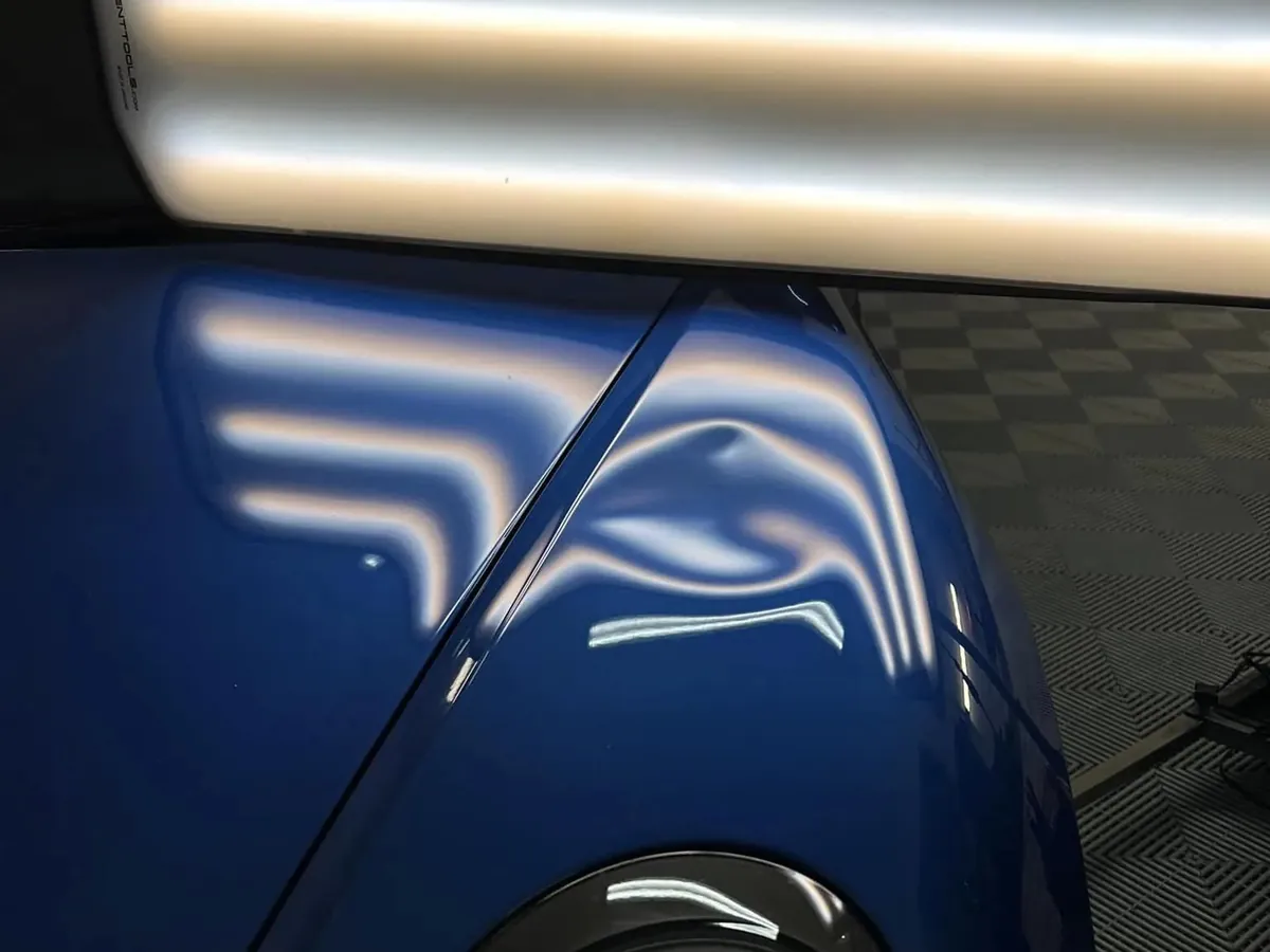 Lampe de débosselage au-dessus d'un impact sur l'aile avant d'une voiture bleue
